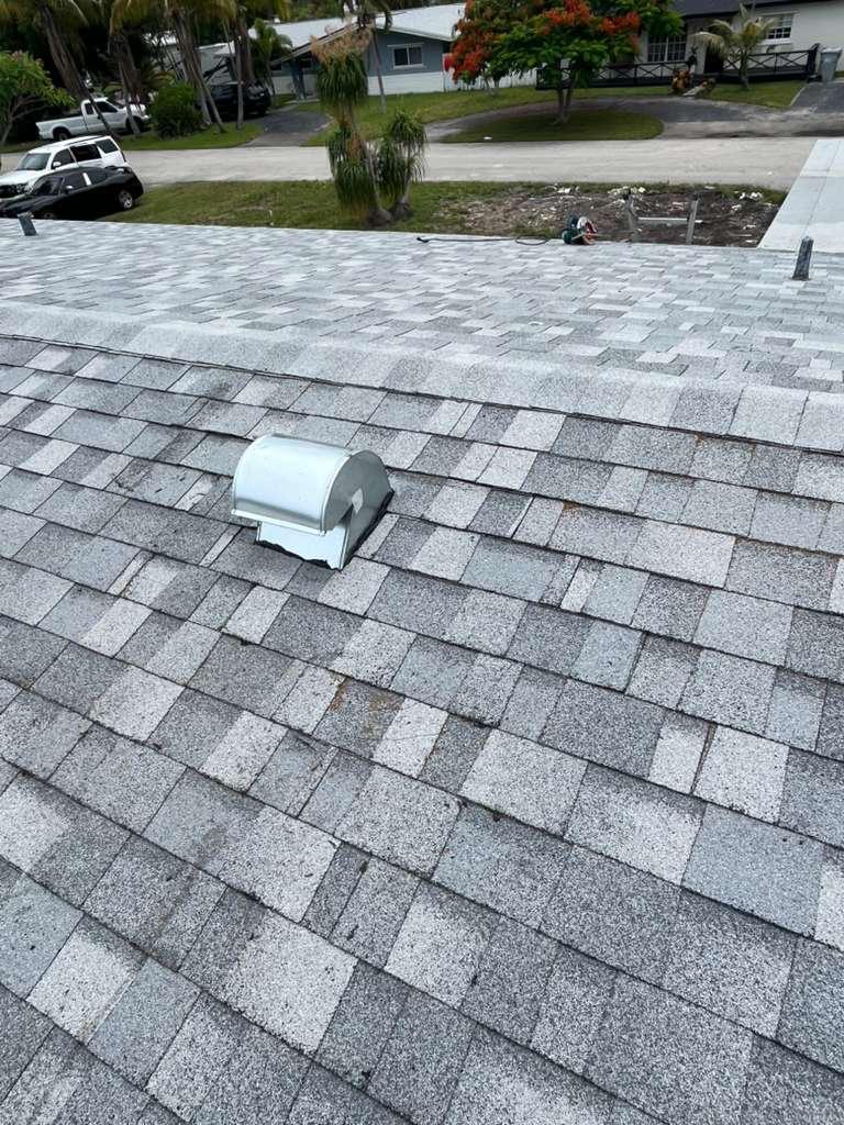 Matching architectural shingles reinstalled around a new kitchen exhaust goose-neck vent on a Broward County roof