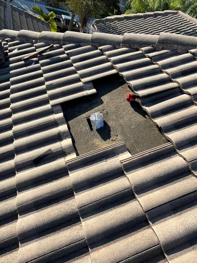 Concrete roof tiles lifted clear of a goose-neck vent opening on a Broward County tile roof, exposing the underlayment and duct stub