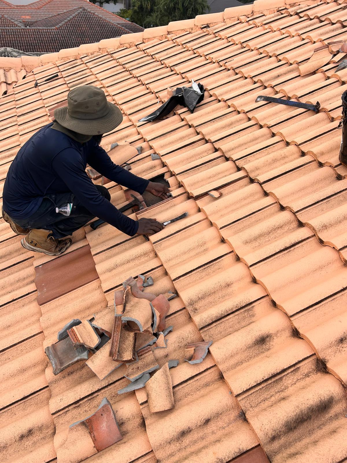 SafeTech roofer removing cracked concrete roof tiles by hand on a Broward County tile roof repair
