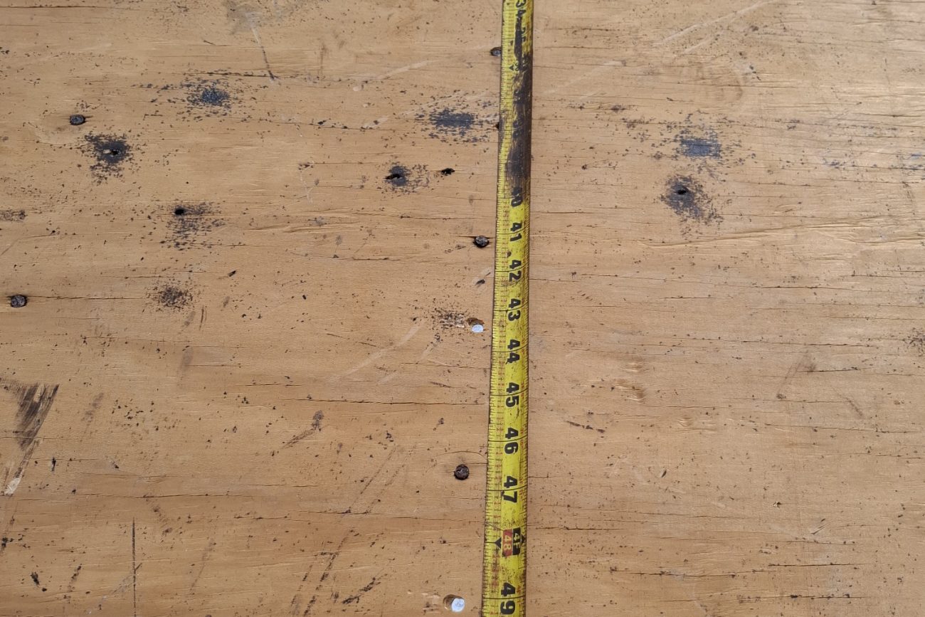 Close view of a tape measure against fastener heads on a plywood roof deck
