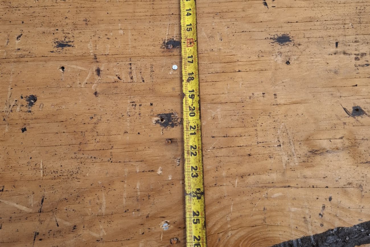 Tape measure on a roof deck beside a bead of mastic during a documented re-roof