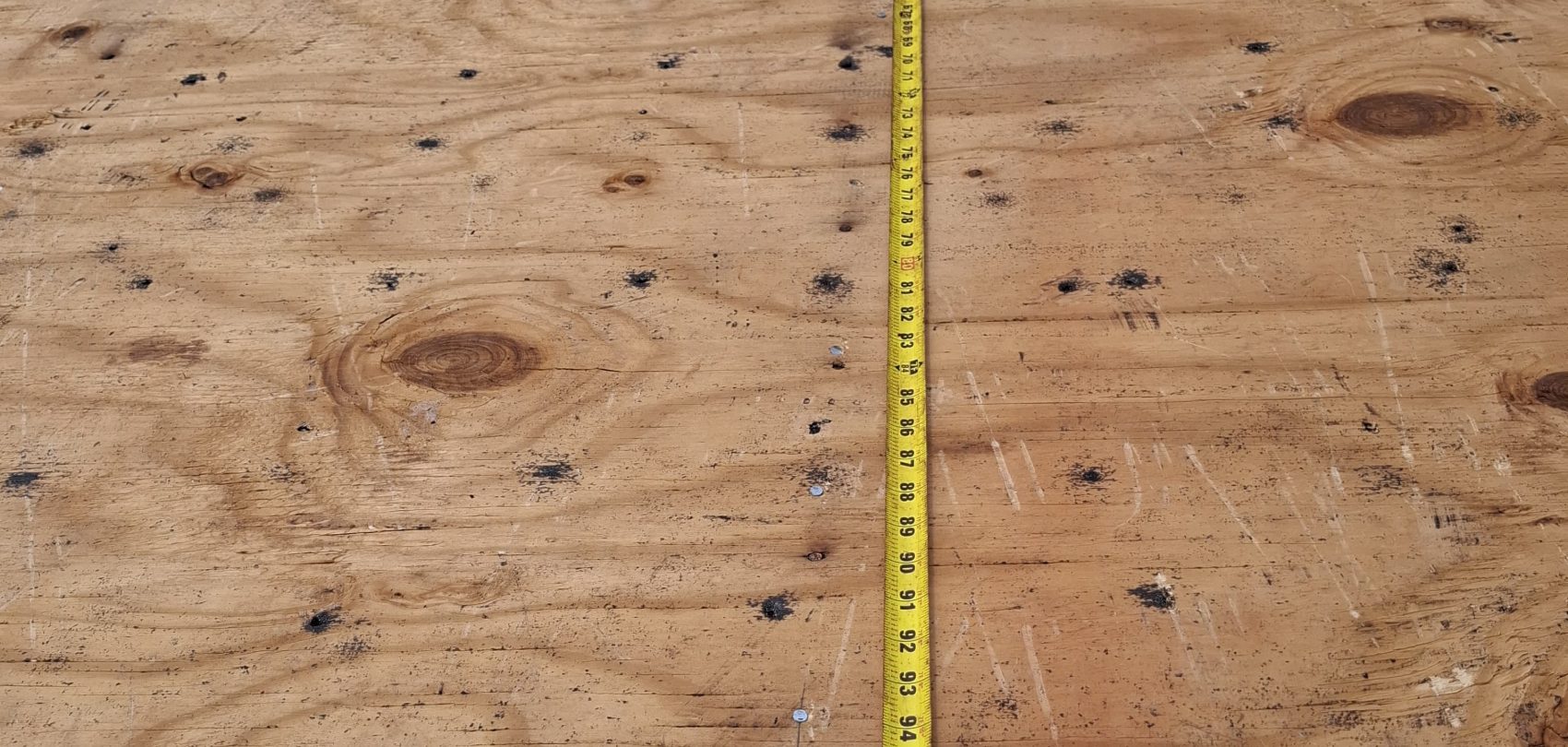 Tape measure laid across a roof deck seam documenting fastener spacing before an inspection