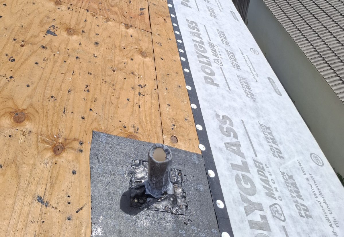 Plumbing vent flashed with a membrane target and sealed, on a roof deck beside a run of underlayment