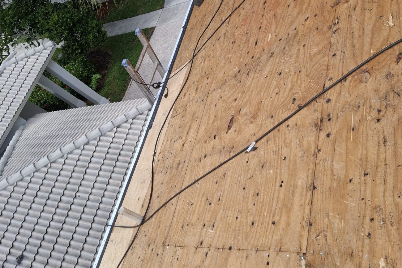 Roofer with a nail gun working along the eave of an exposed plywood roof deck