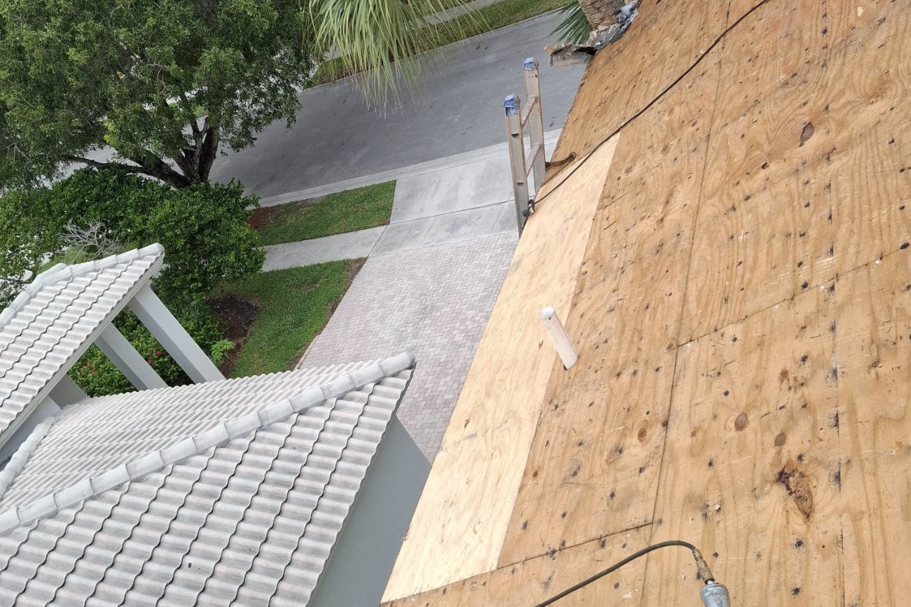 Bare plywood roof deck exposed after tile tear-off, with a nail gun and air line on the slope