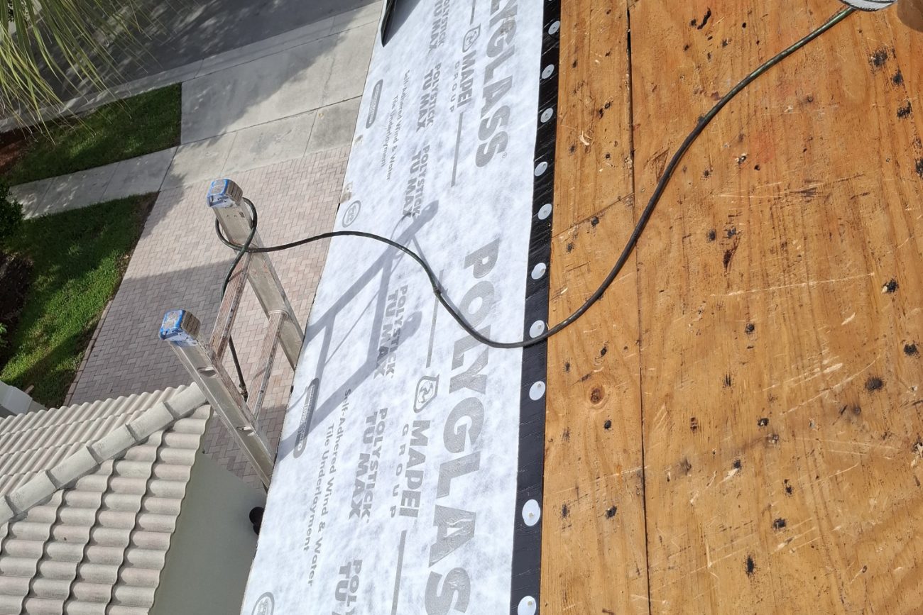 Roofer rolling out self-adhered Polystick TU MAX underlayment along a roof deck