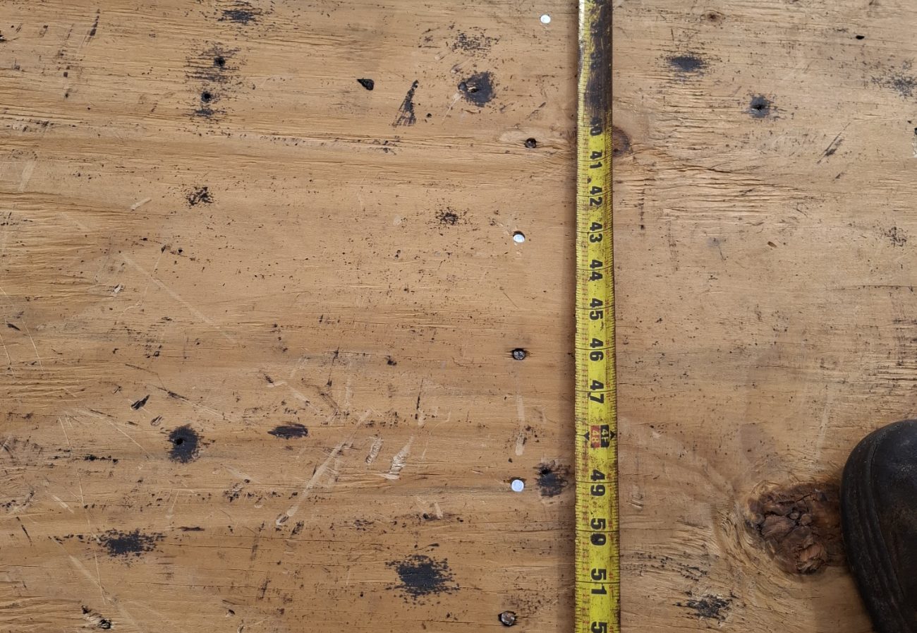 Tape measure laid along a plywood roof deck documenting nail spacing during a re-roof