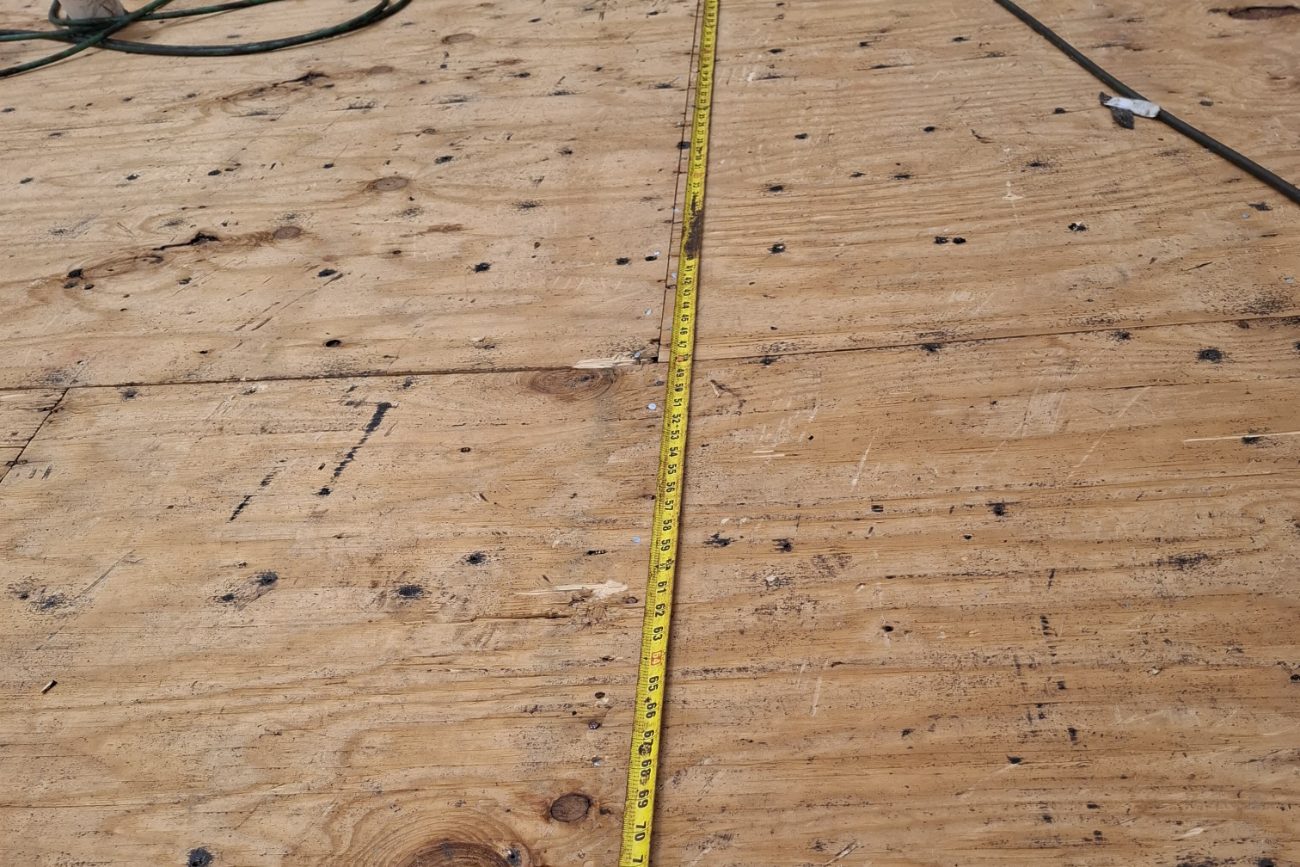 Tape measure documenting fastener spacing on a roof deck, with a neighbouring tile roof beyond