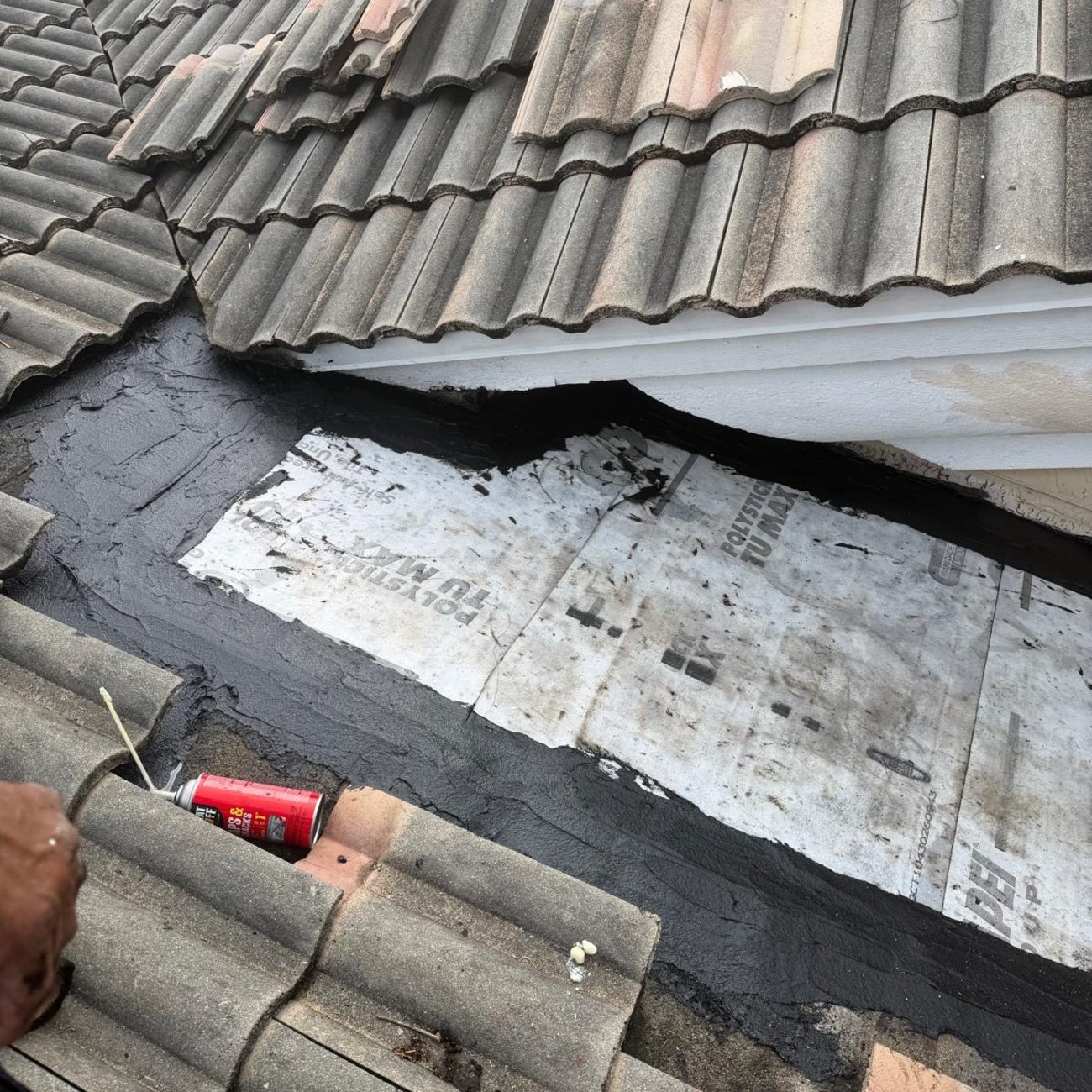 Tile lifted to reveal weathered underlayment patched with black mastic at a roof valley