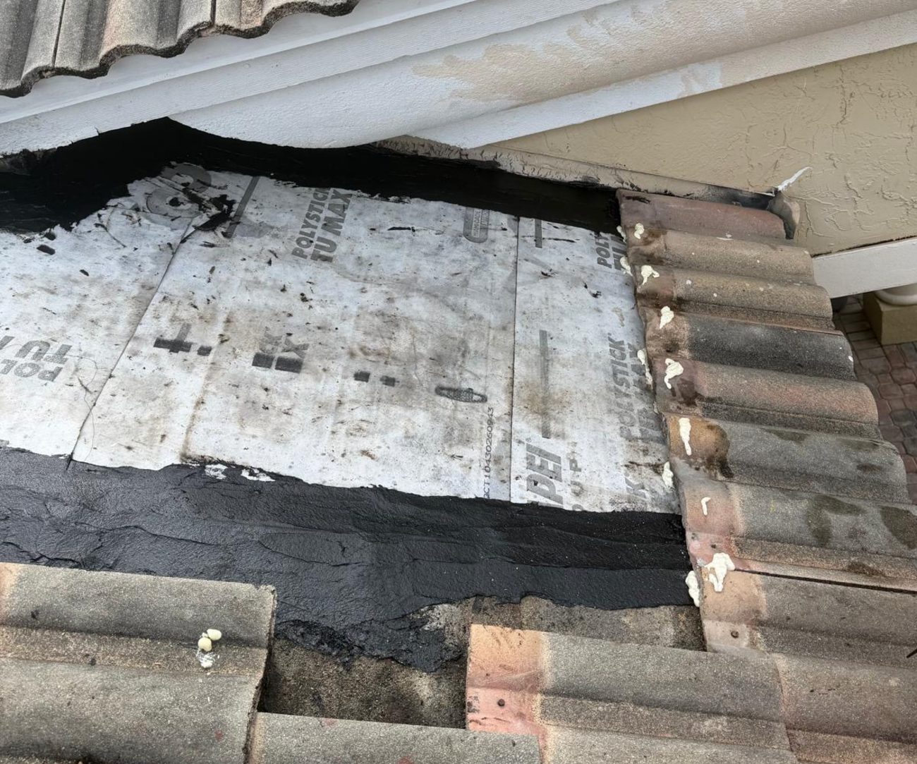 Weathered self-adhered underlayment exposed beneath lifted tile, streaked with old mastic