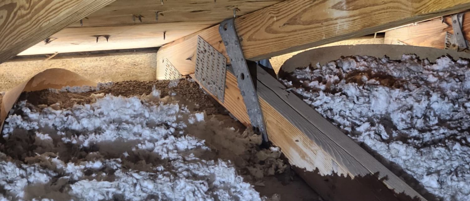 Attic wall line where blown-in insulation has drifted over the truss connections and ventilation baffles