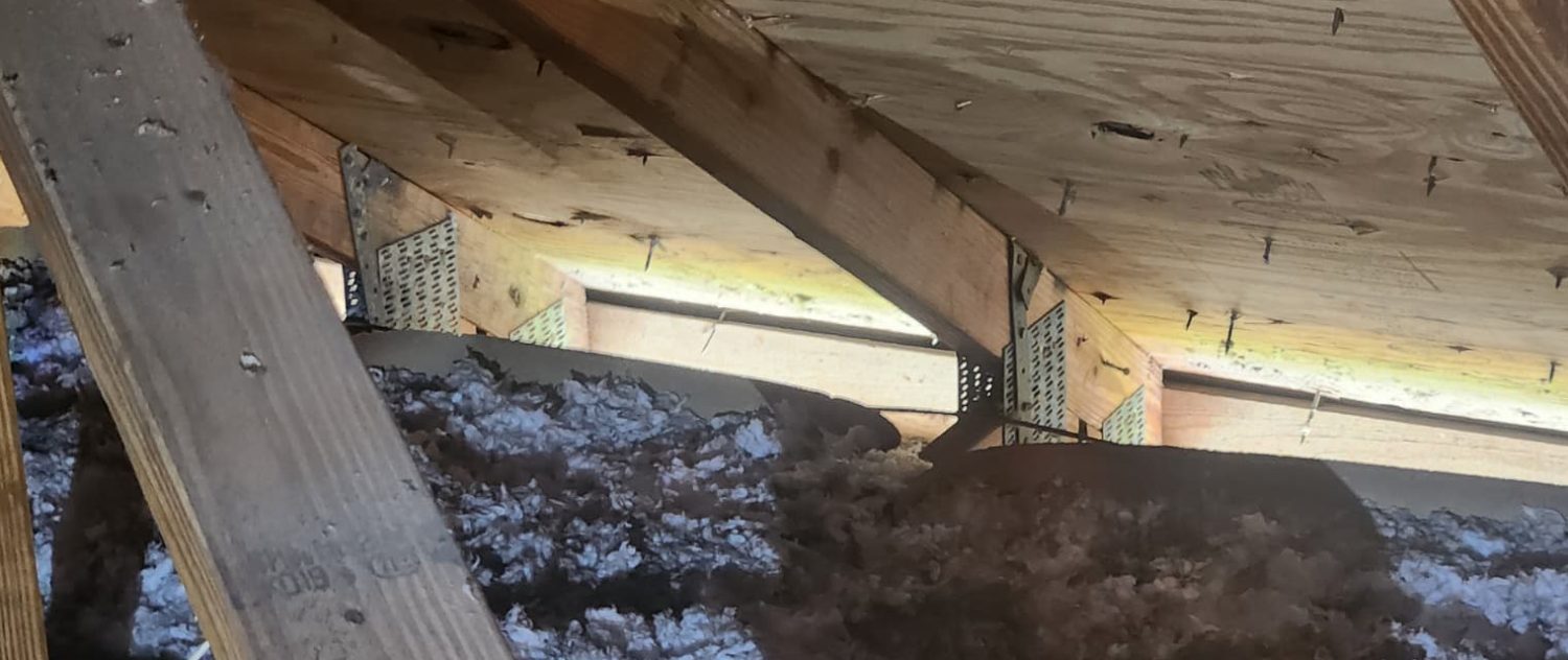 Truss heel resting on a wall top plate with a metal connector and pressed gusset plates, seen from inside the attic