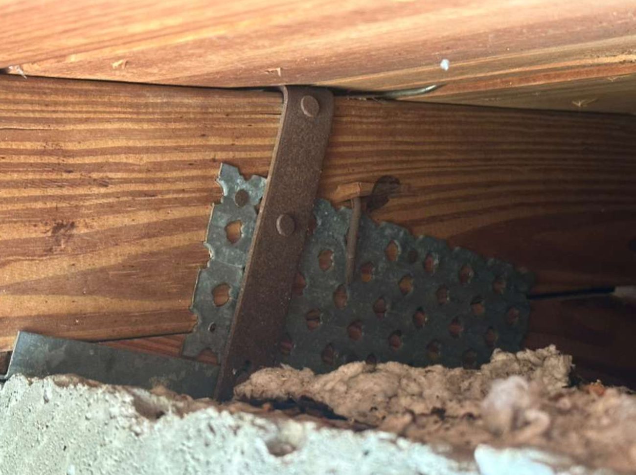 Close-up of a metal strap passing over the top of a roof member and down its face, above a concrete tie beam