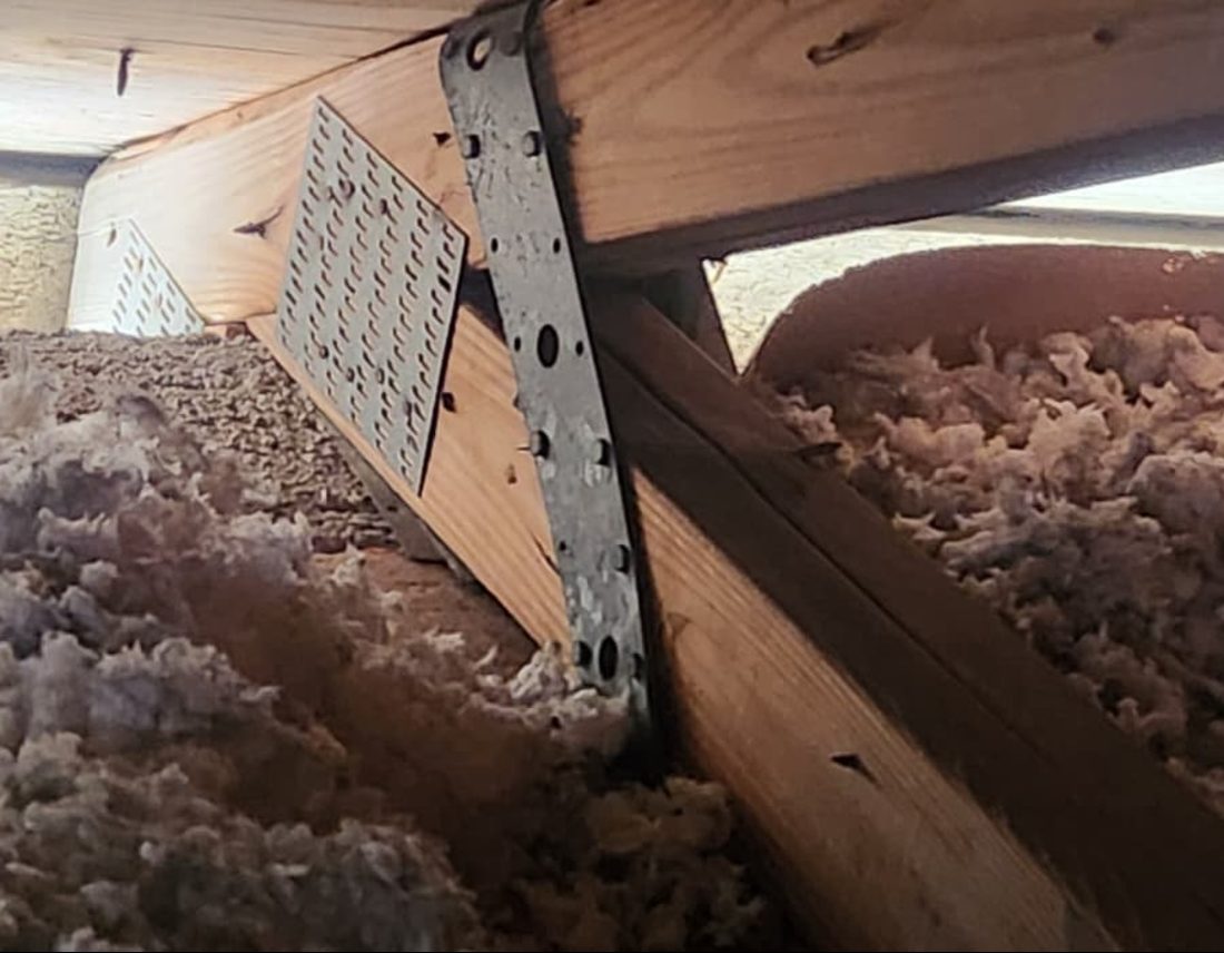 Metal strap over the top of a truss at the wall line in a blown-insulation attic