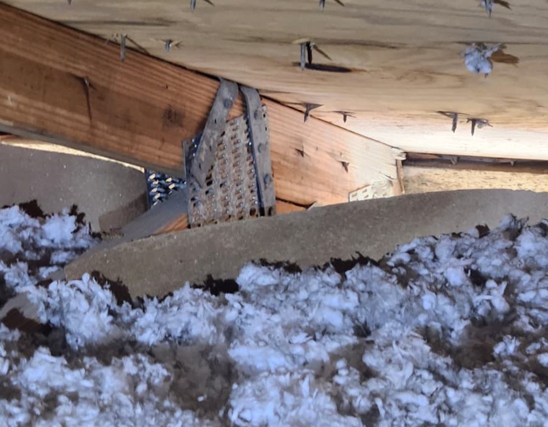 Two adjacent truss heels with metal connectors and pressed plates above blown-in attic insulation